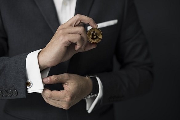 Мужчина в костюме держит в руке биткойн